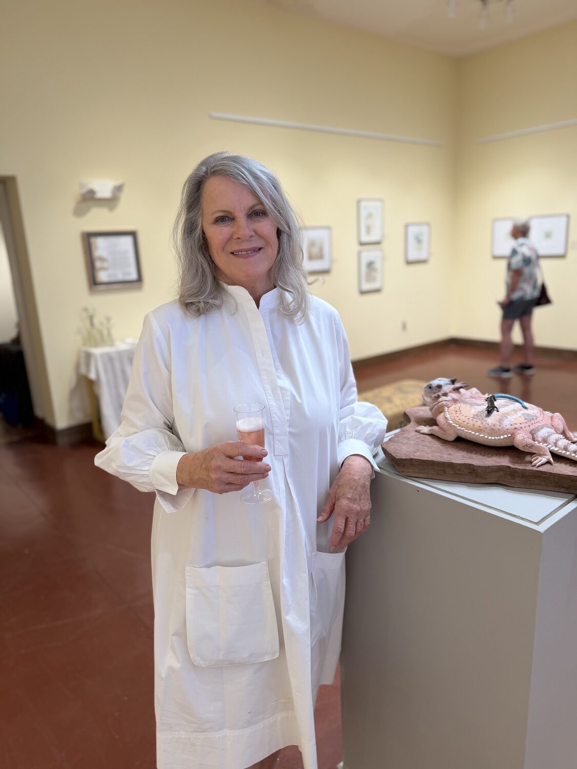 Cathe Bloomfield Collard at the opening reception, standing beside her horned-lizard box sculpture with framed watercolors on the gallery wall behind her
