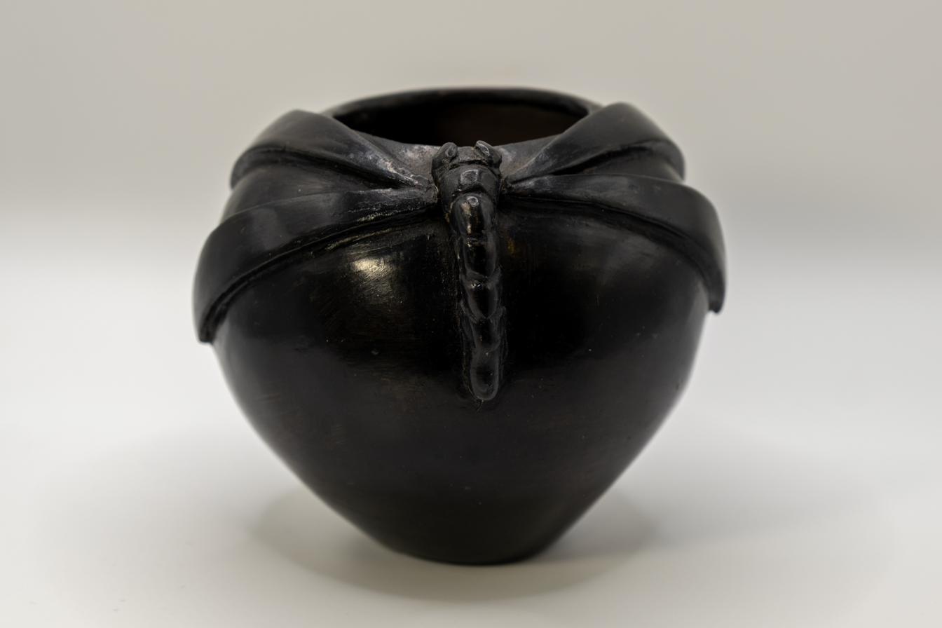 Dark pit-fired terracotta vessel with a wide, rounded body and a sculpted dragonfly perched across its pinched, gathered rim