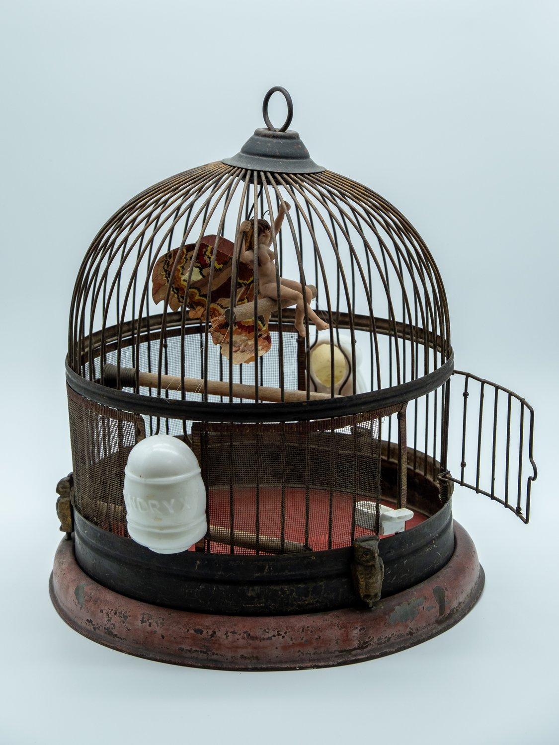 Mixed-media sculpture of a small winged fairy figure with pressed cottonwood-leaf wings, perched inside an antique domed birdcage