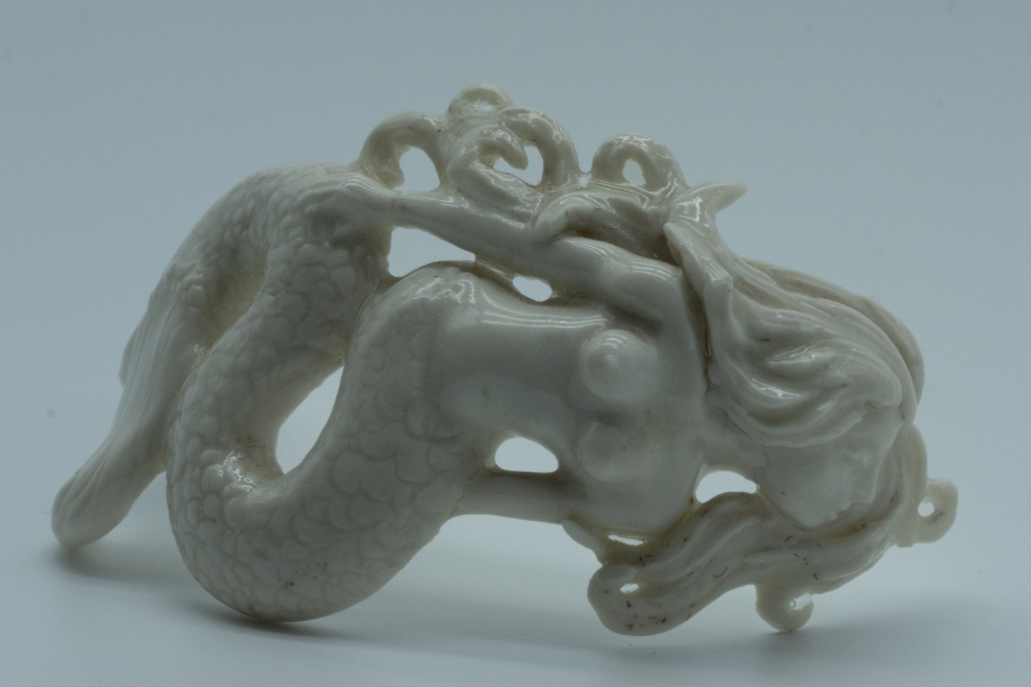 White glazed porcelain choker necklace carved as a mermaid-like creature with a scaled, curling tail and flowing hair wrapped around a rounded form