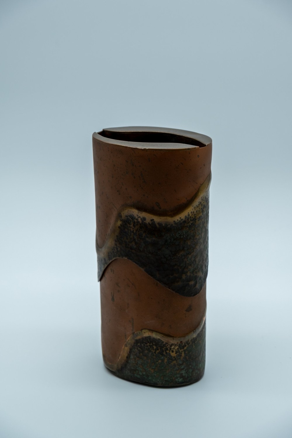 Repoussé copper box with a rounded, river-stone-like form, its surface worked into a wave pattern with patches of dark oxidized patina against burnished copper