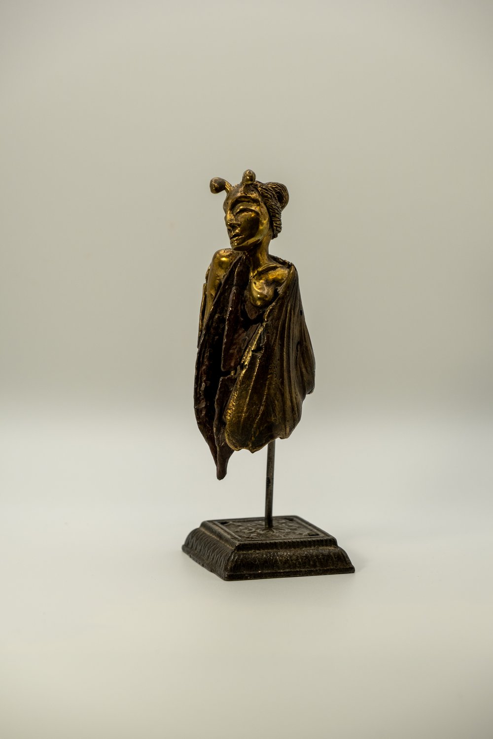 Small bronze sculpture of a fairy figure emerging from a pod-like wrap, mounted on an ornate metal stand