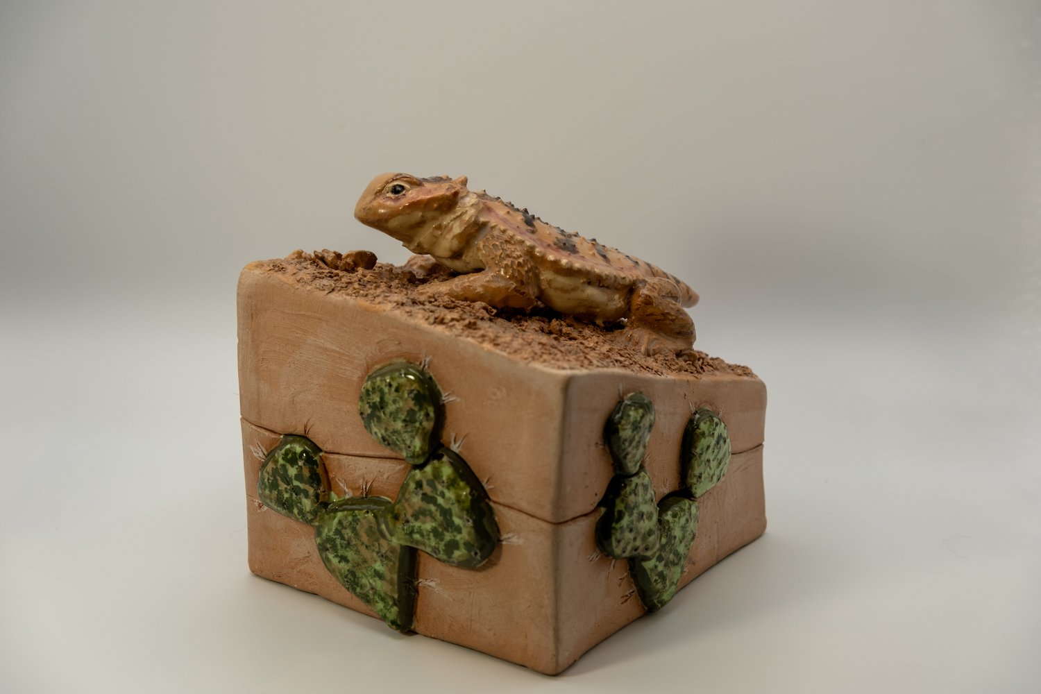 Terracotta box with a sculpted short-horned lizard resting on a sandy top, the sides decorated with glazed prickly-pear cactus pads