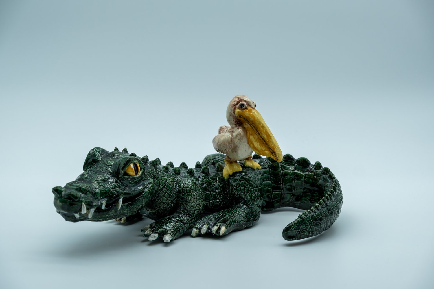 Glazed ceramic sculpture of a green alligator lying down with a white pelican perched on its back