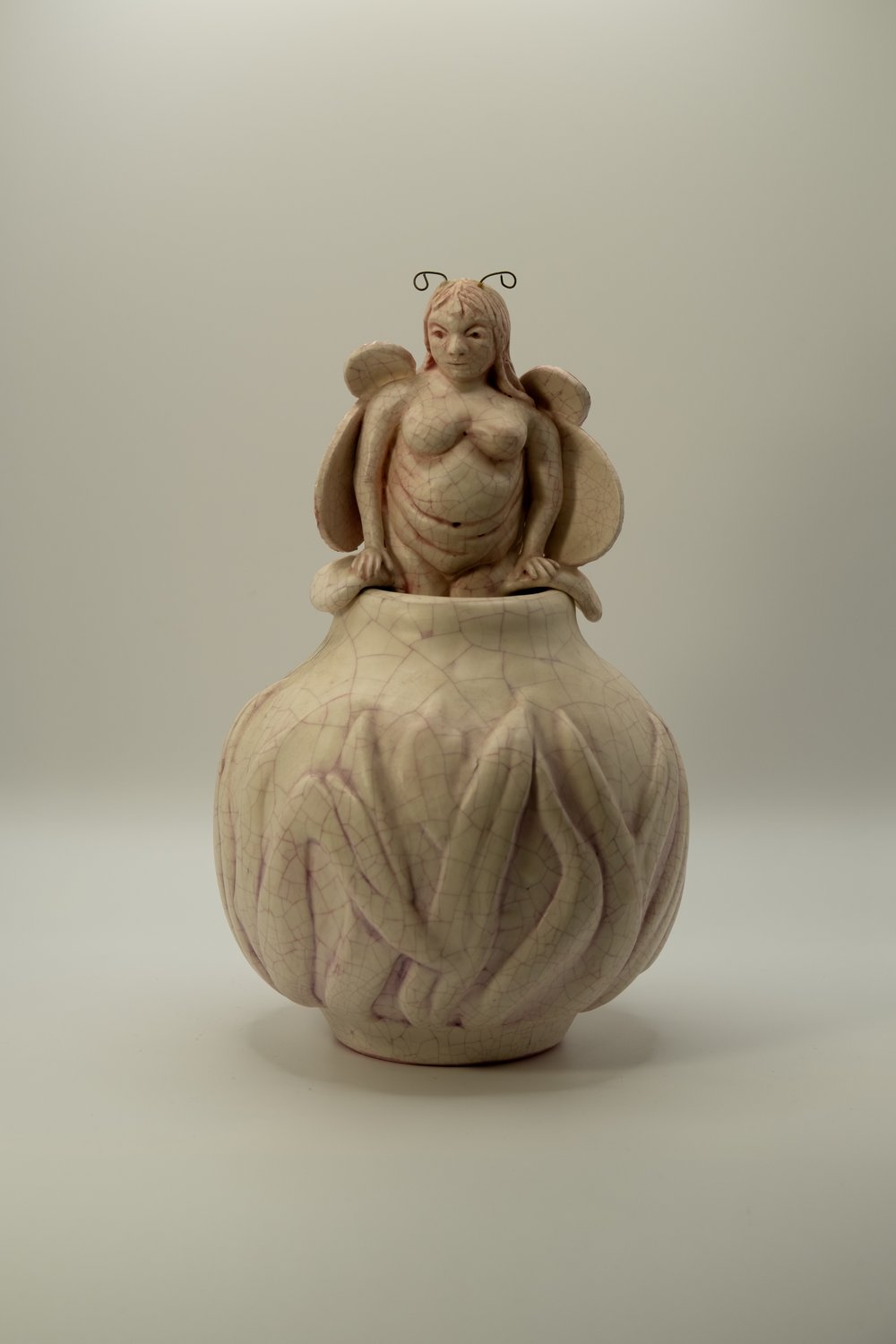 Carved porcelain sculpture of a winged fairy figure with antennae emerging from a tall crackle-glazed pot
